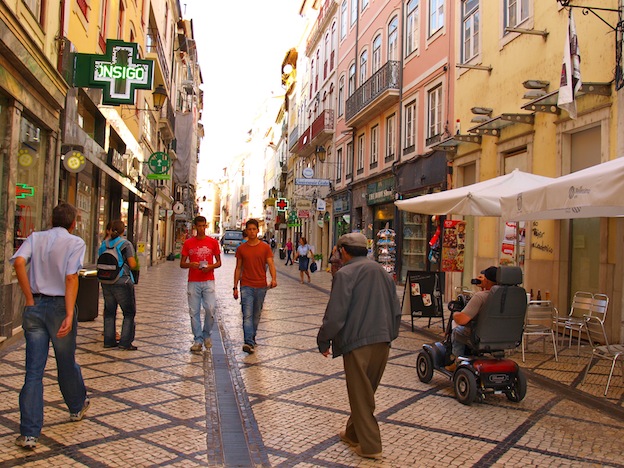 calle en coimbra con personas paseando y un scooter eléctrico con una persona con discapacidad