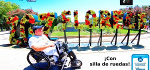 Miguel con su silla de ruedas junto al cartel de Zaragoza Florece